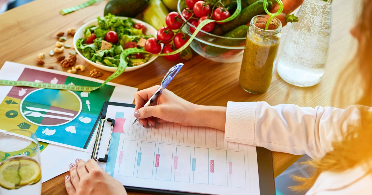 An overhead view of someone writing on a clipboard beside fresh foods and a measuring tape, suggesting nutrition planning for Weight Loss Programs in Tracy, CA.